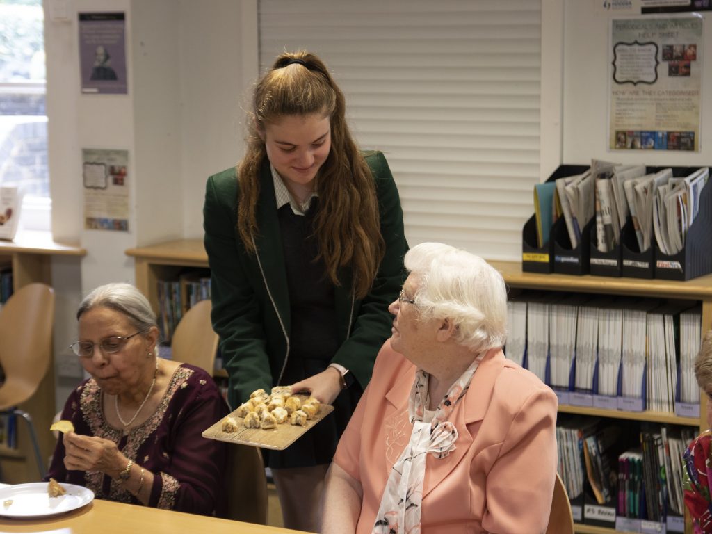 student offering sausage rolls to a woman