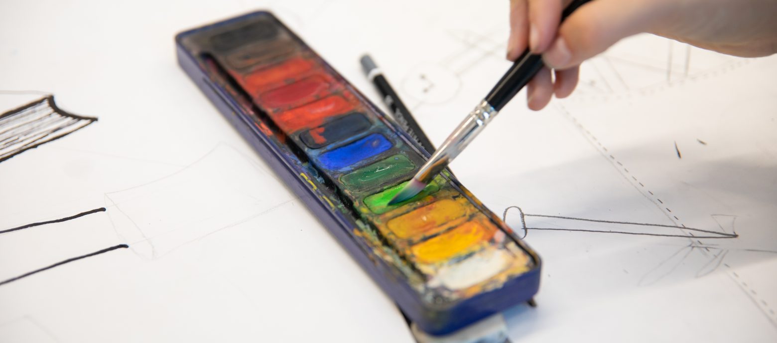 student dipping paintbrush into watercolour palette
