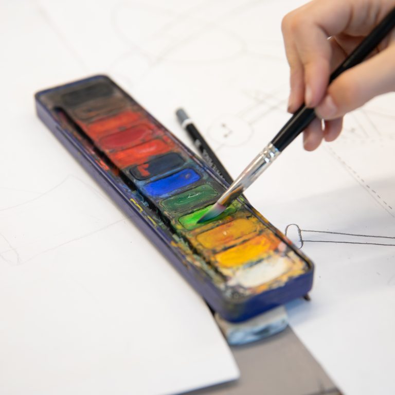 student dipping paintbrush into watercolour palette