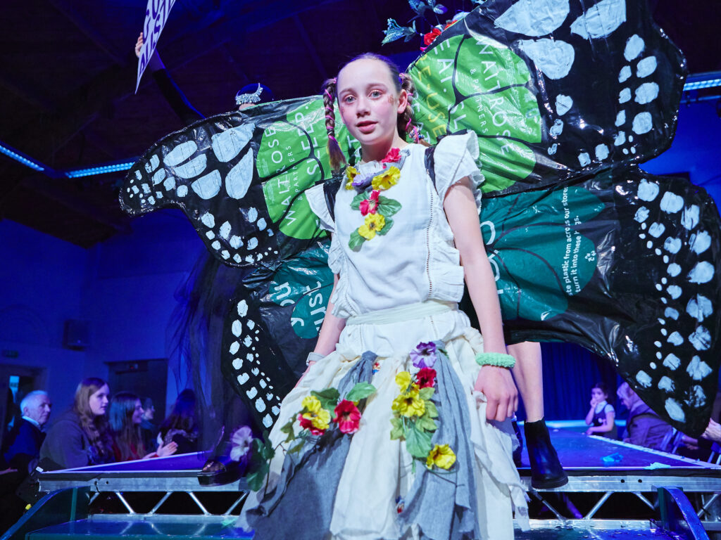 Girl in colourful outfit with butterfly wings on catwalk