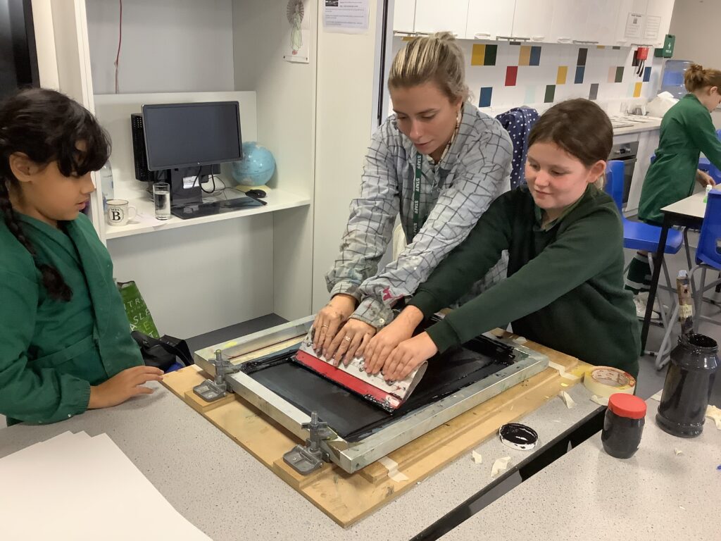 Teacher showing 2 school girls how to screen print