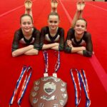 Three girls laying down on red carpet with a selection of medals